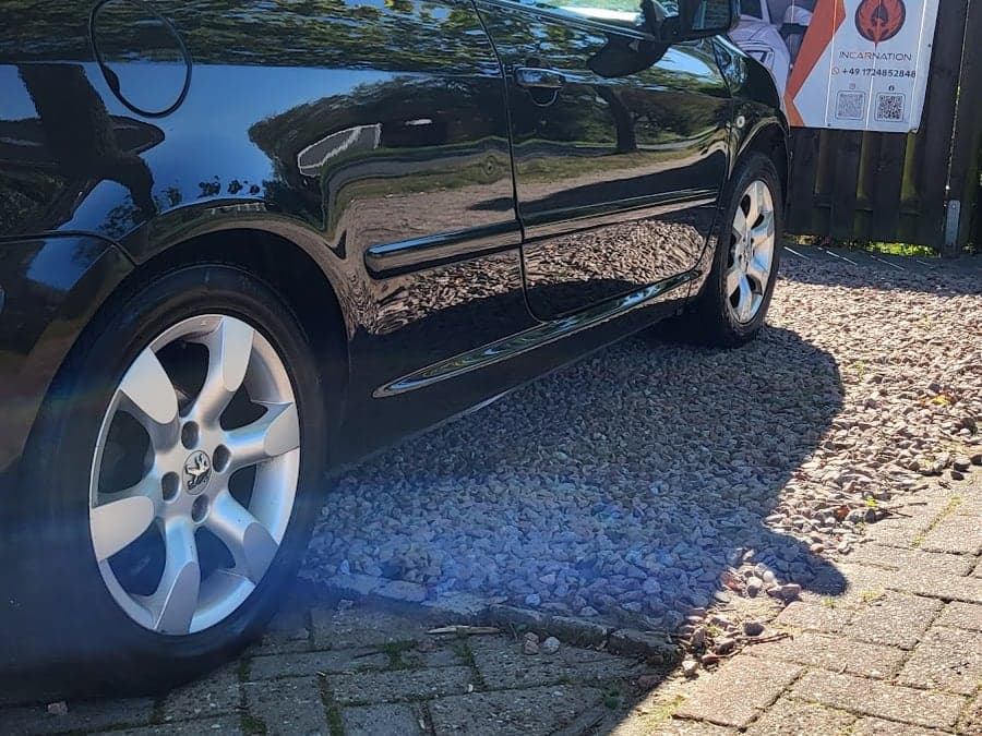 Schwarzes Peugeot Coupé vor dem Incarnation-Banner des Betriebs